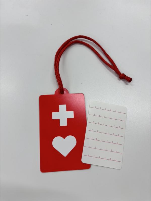 ライメックスという素材で作られた、新しいヘルプマークの画像。薄いカード型をしていて、バッグ等に結ぶ用の赤い紐が付いている。