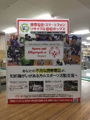 「携帯電話・スマートフォン リサイクル回収ボックス」と書かれた回収ボックスが、机の上に乗っている写真