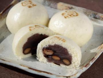 四角い焼き物のお皿におまんじゅうが3つ乗っており手前の一つは半分になり中身のあんこが見えている写真