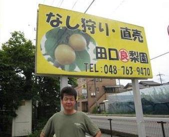 なし狩り・直売 田口良梨園と書かれた看板の前に立つ男性の写真