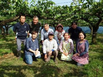 梨園の樹木を背に生産者のみなさんが並んで記念撮影している写真