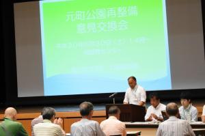 スライドショーを背に話している男性と、座って聞いている人たちがいる、意見交換会の様子の写真