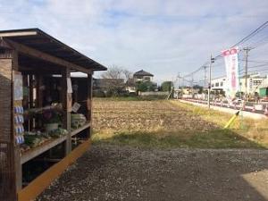 畑の隣に、農産物が並んだ棚が建っている写真