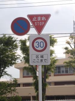 赤地に白で「止まれ」と書かれた標識の下に赤丸の中に青い文字で「30」と書かれ、「区域ここまで」と記載された標識の写真