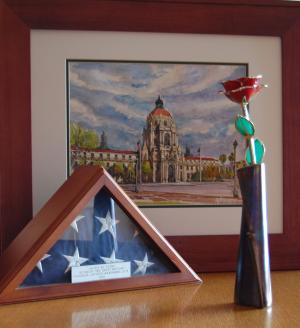 卓上に展示された記念品の数々の写真。バラの花をかたどった記念品、木製の額に収められたパサディナ市の市庁舎の絵、折り畳まれた状態で三角形の木製ケースに収められたアメリカ合衆国の国旗等が並べられている