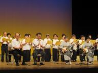 ステージ上で高齢者の方々が楽器を演奏し歌を唄っている、福祉大会の様子の写真