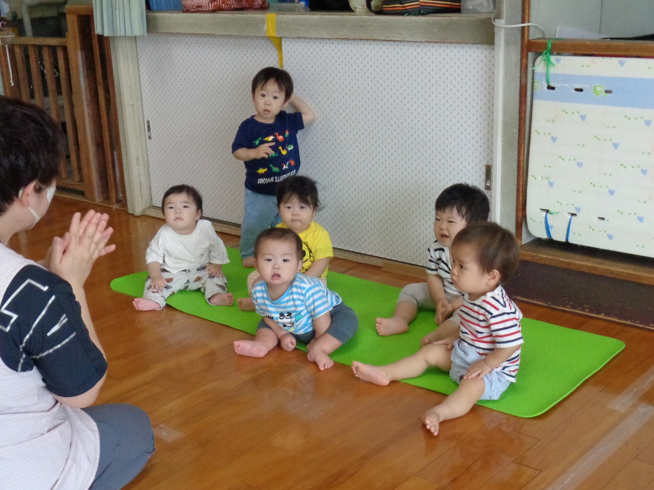 保育所室内で園児達が、保育士の手の動きを見ながら歌遊びを楽しんでいる様子の写真