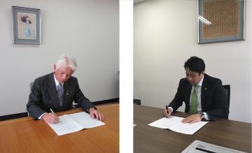 スーツ姿の男性が机に向かって協定書にサインしている、大塚製薬平内大宮支店長と石川市長の写真