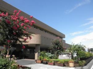 ピンクの花や植木の奥に大きな建物が見える、春日部市第5地域包括支援センターの外観の写真