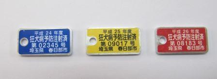 左から青色、黄色、赤色のプレートが並び、それらに白色の文字で情報が記載された狂犬病予防注射済票の見本写真