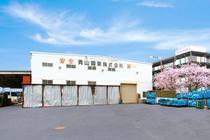 2本の桜の左に建てられた青山鋼業 株式会社の外観の写真