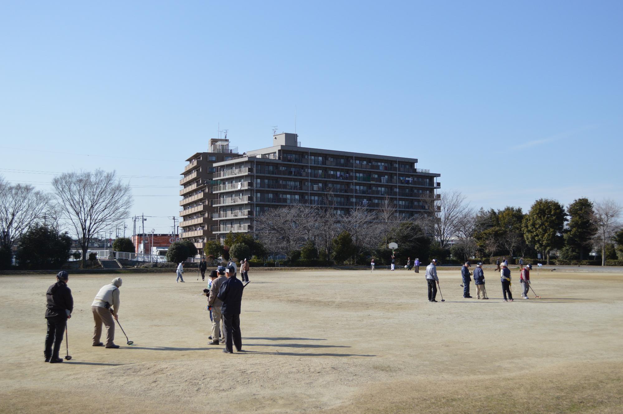 青空の下そびえるマンションを背景に公園で遊んでいる人たちの写真