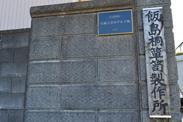 コンクリートの外壁に立てられている飯島桐たんす表札の写真