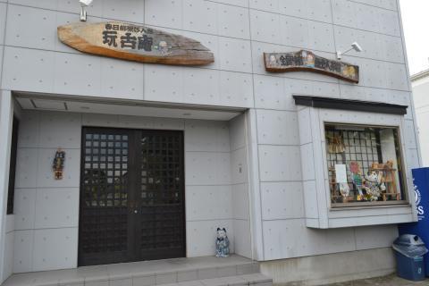 コンクリート地の建物に木の看板が掛けられている玩古庵正面入口の写真