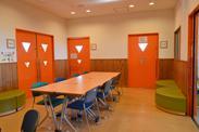 明るいオレンジの扉と木を基調にした部屋が特徴的な交流スペースの写真