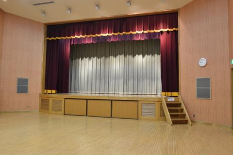 赤い幕が開かれた状態の多目的ホールのステージの写真