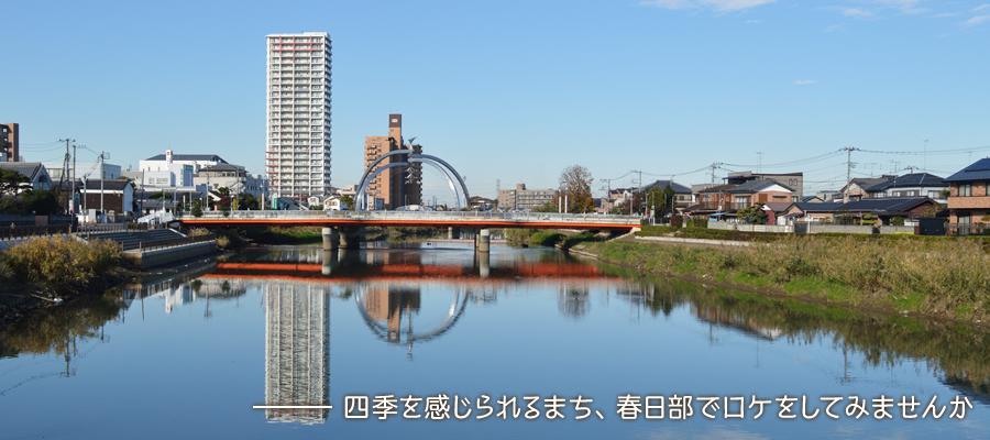 青空の下、市街地が広がり奥に橋が見える川面からの写真「四季を感じられるまち、春日部市でロケをしてみませんか」