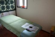 柔らかいグリーンの色合いのベッドと植物のタペストリーが特徴的な施術室の写真