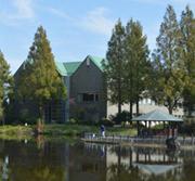 針葉樹や湖の緑に溶け込むように建つ緑色の三角屋根の庄和総合支所の写真