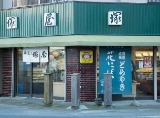 菓匠 塚屋と書かれた白い暖簾がかかる店舗入り口を斜め右から写した正面写真