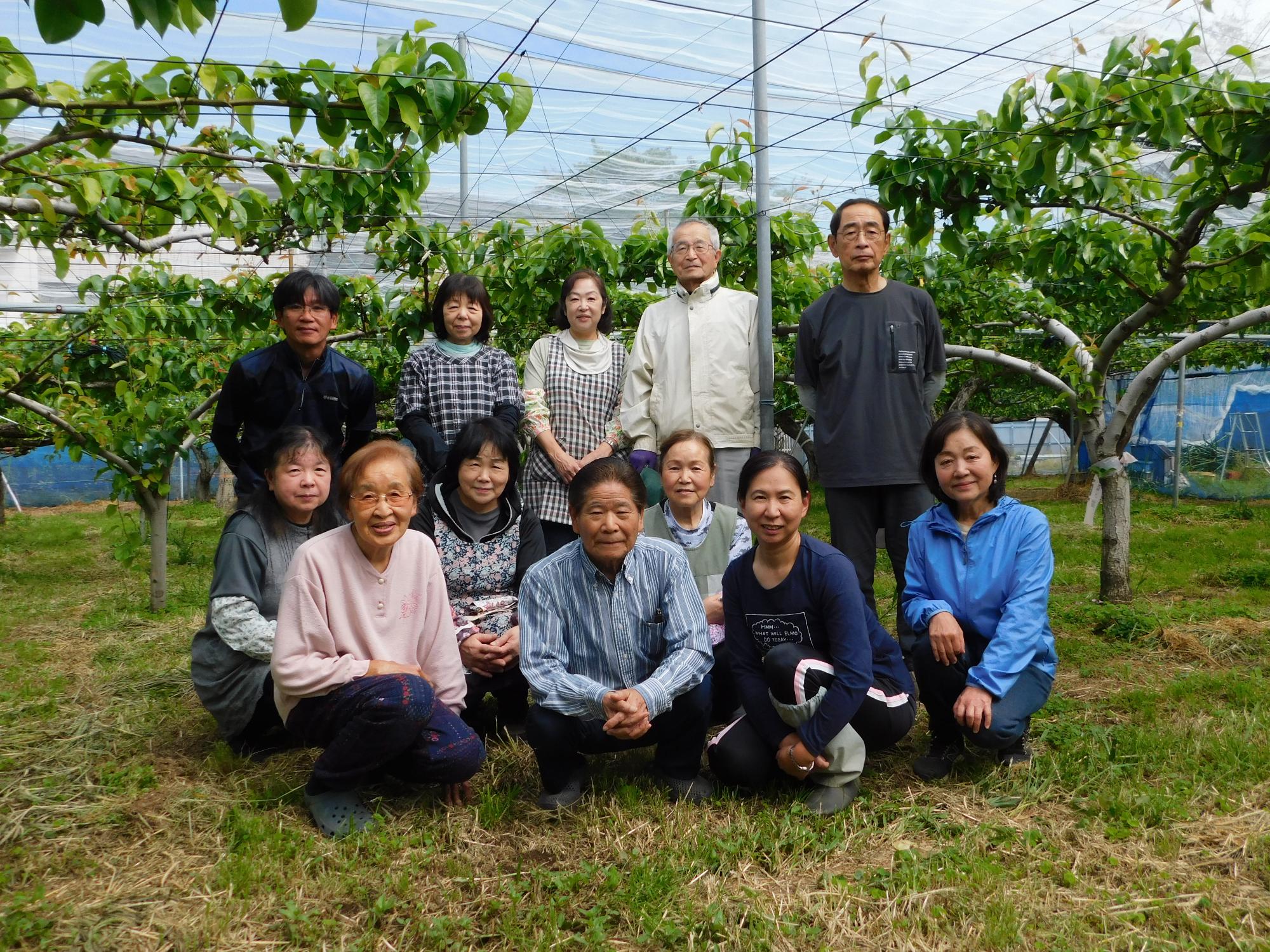 梨園の樹木を背に生産者のみなさんが並んで記念撮影している写真