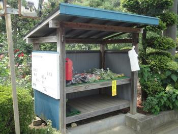 木でできた屋根付きの棚に野菜が並べて売られている直売所の写真