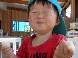 赤いTシャツを着た男の子が笑顔で梨を食べている写真