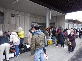 市内の農家さんが集まり自慢の新鮮な野菜を一列に並べ、お客さんが選んでいる写真