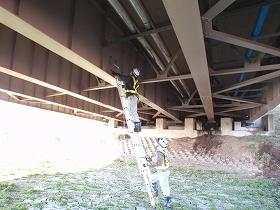 橋梁下部を梯子を用い点検する作業員の写真