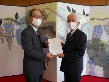 藤の絵が描かれた屏風の前で、審議会の男性から答申を受け取る石川市長の写真