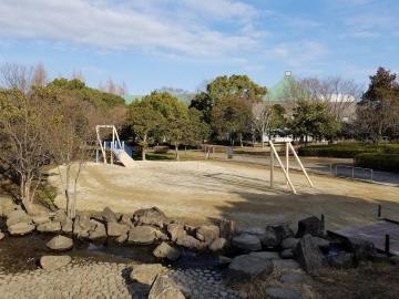 手前に川が流れている、新しくなった庄和総合公園遊具広場の全景の写真