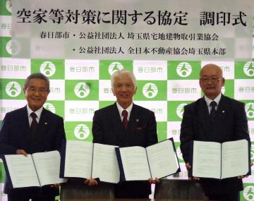 空家等対策に関する協定調印式で、石川市長を真ん中にして両脇に両協会の支部長と計3人が横に並び、締結書を開いて見せながら笑顔を浮かべる様子を撮影した写真