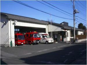 春日部消防署備後分署の1階建ての建物とその横に1階建ての車庫の建物があり、車庫に消防車2台と救急車1台が並んでいる様子の写真
