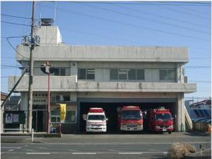 春日部消防署浜川戸分署の2階建てコンクリートの建物の1階入り口の横に車庫があり、車庫に1台の救急車と2台の消防車が並んでいる様子の写真