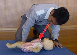 呼吸の確認のため赤ちゃんの人形の胸部や腹部を観察している男性の写真