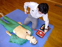 電極パッドをマネキンに繋いで、AEDの操作を行う男性の写真