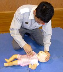 赤ちゃんの人形の額を押さえながら心臓マッサージの準備をする男性の写真