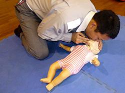 赤ちゃん人形に人工呼吸をする男性の写真