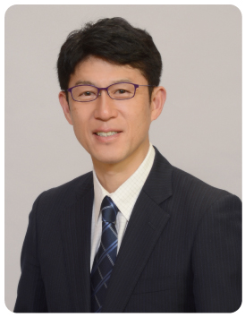 黒色のスーツに紺のストライプ柄のネクタイをつけ笑顔の平井 信行さんの写真