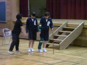 体育館で児童が足に重りを付けて杖をつきながら歩いている写真
