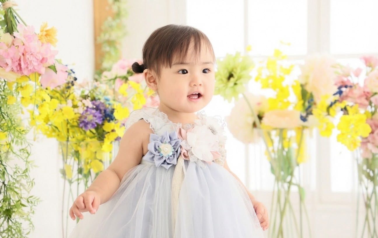 黄色を主体に色とりどりの花に囲まれ、薄水色のドレスを着た女の子の写真。