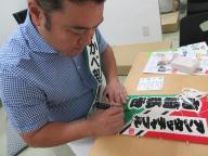 机に向かってマジックペンで凧にサインを入れる山崎さんの写真