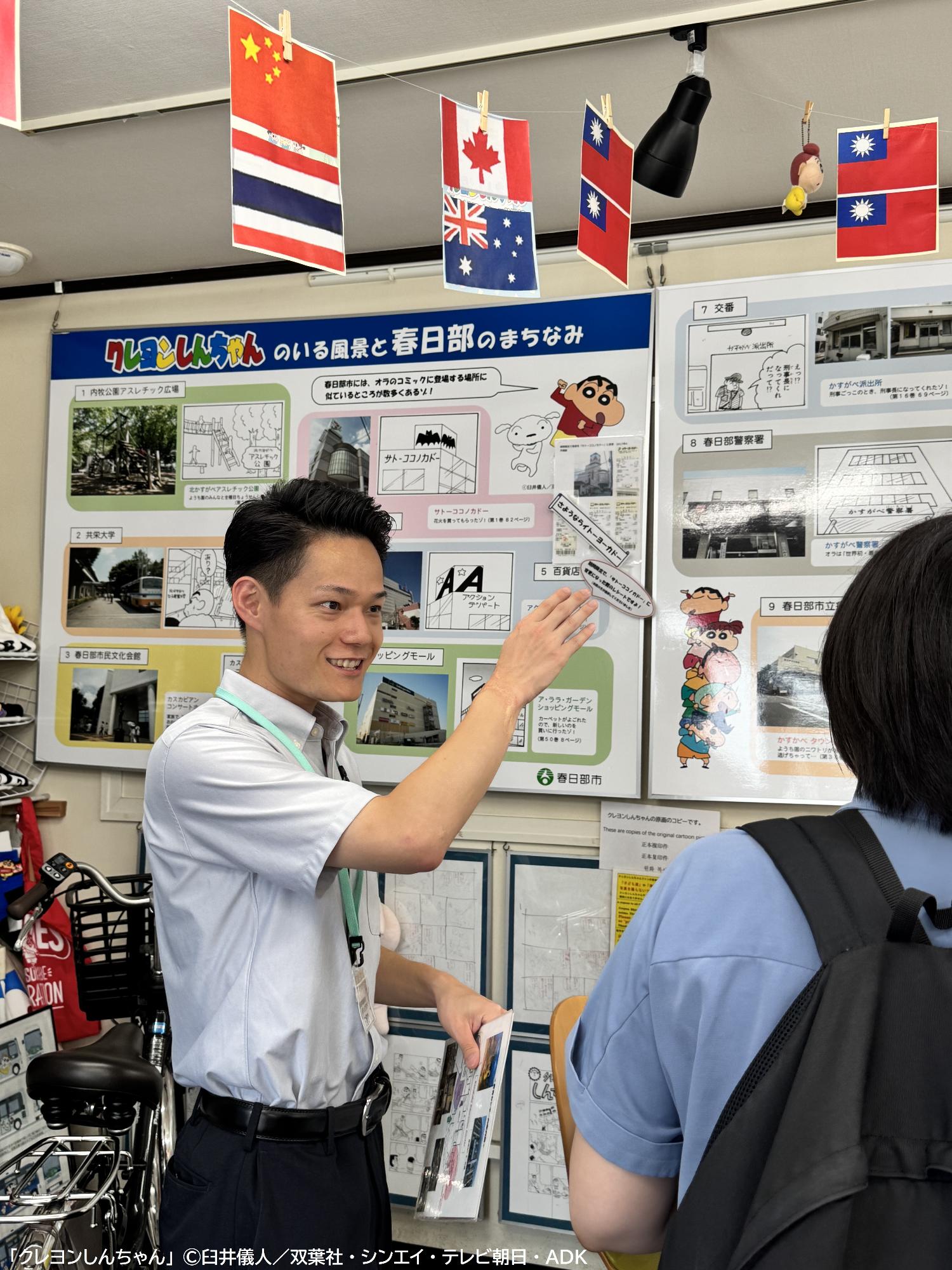 日留田さんが施設内の展示ボードを用いて青色のシャツを着たお客様を案内している様子。
