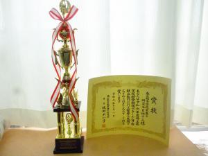 金色のトロフィーと賞状が並べて置かれている写真