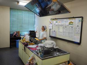 炊飯器やお皿が並んだ調理台の傍で説明している女性の写真