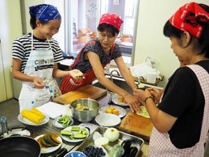 エプロンとバンダナを付けた参加者たちが楽しそうに料理を作っている写真