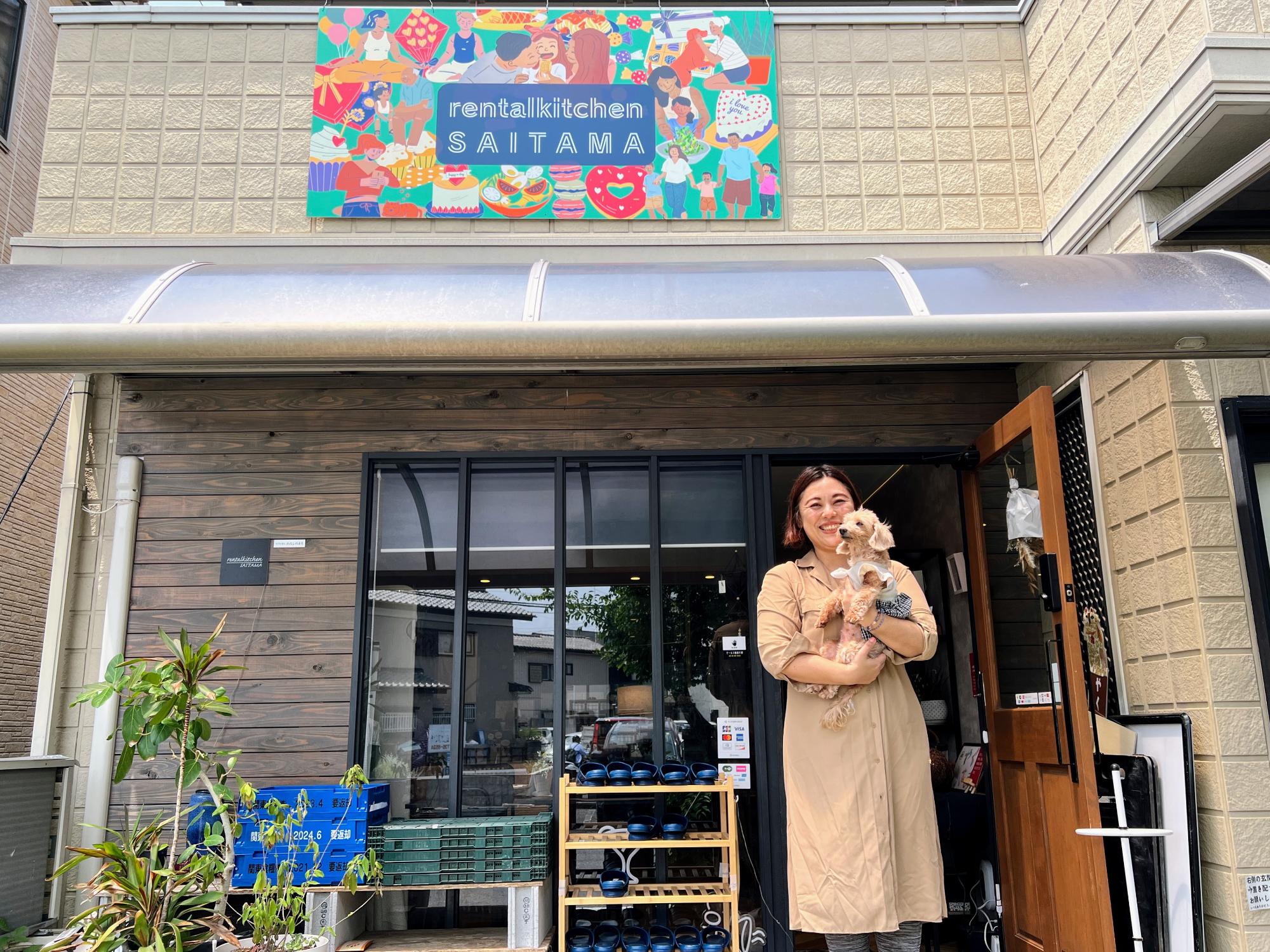 「レンタルキッチンSAITAMA」の店舗前で愛犬を抱きかかえほほえむおおさとさん