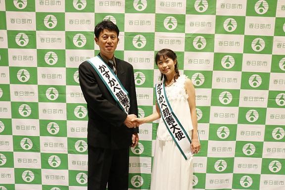 スーツ姿の平井さんと白いワンピース姿のあえかさんが握手をして記念撮影している写真