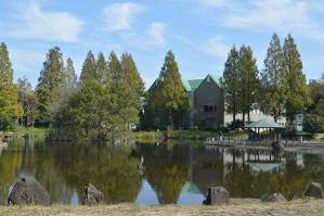 湖の向こうに、木立や三角屋根の建物が見える、庄和総合公園の写真