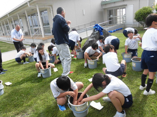 屋外での授業でバケツの中にある土に触れる児童たちの写真